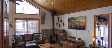 The living room features a large leather sofa, love seat, wood stove, and 4K TV.