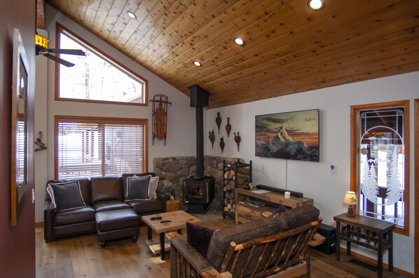 The living room features a large leather sofa, love seat, wood stove, and 4K TV.