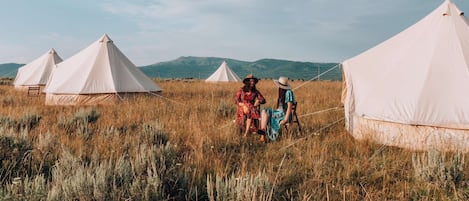 Two campers visiting in the field with mountains views outside of our waterproof, canvas bell tents with low profile windows and large netted, double zipper doors at our Yellowstone camp.