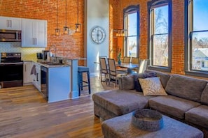 Ample natural light with large windows and an open floorplan between kitchen, living room, and dining space.