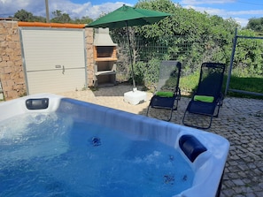 Jardim com jacuzzi, espreguicadeiras e barbecue.