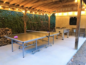 Outdoor covered game area includes ping pong, foosball and cornhole.