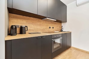 A modern kitchenette with sleek dark cabinets, a wooden countertop, and appliances including a kettle and coffee machine.