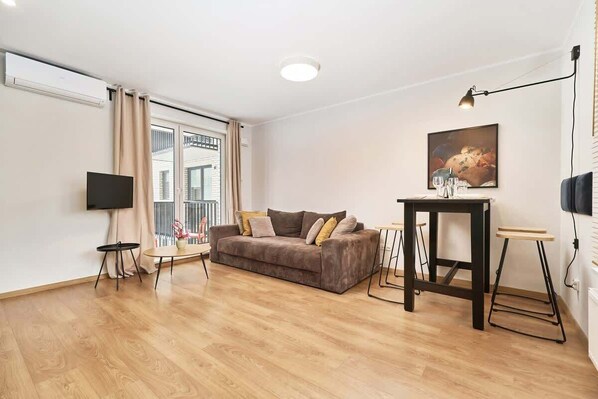 A spacious living area with a brown sofa, a wooden coffee table, and large windows that provide plenty of natural light. Decorated in warm, neutral tones for comfort.