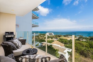 Balcony with comfortable chairs, table and gas BBQ grill.  Ocean view.