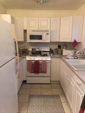 Cozy kitchen w gas stove and several small appliances and plates, cups, utensils