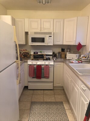 Cozy kitchen w gas stove and several small appliances and plates, cups, utensils