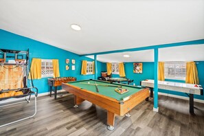 Game On Central! 🎮🌟🏡 - A fully equipped game room featuring a pool table, foosball, poker table, and basketball setup for a diverse and thrilling leisure experience.