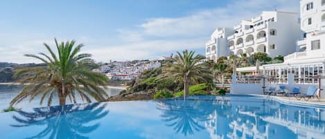 Tranquil pool reflecting the sky, with striking palm silhouettes and white architecture.