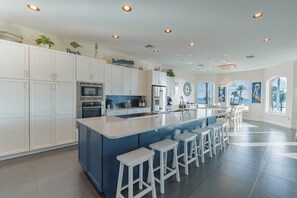 This modern coastal kitchen features sleek finishes, calming blue accents, and an oversized island that comfortably seats 8..