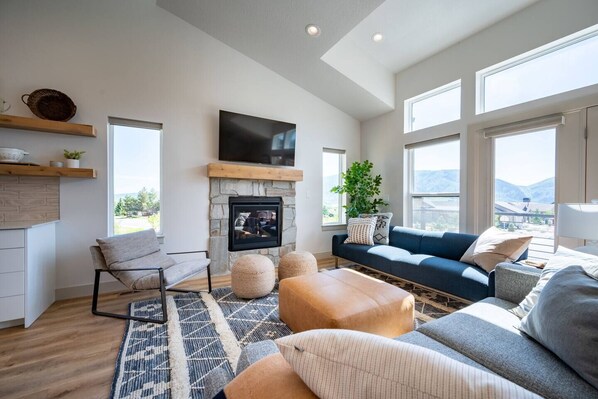 The living room, freshly appointed with comfy furniture, a smart TV and fireplace, offers easy access to the outdoor deck and spectacular views.