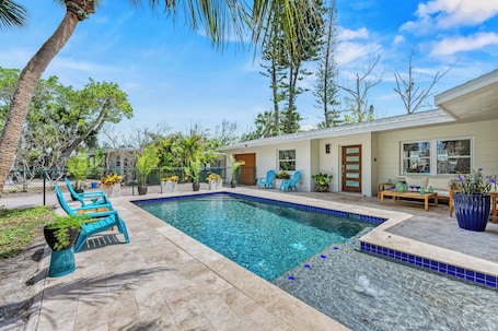 The pool boasts a baja shelf for a water immersed tanning. Patio with lounge area, chaise lounges, and additional seating areas surround the glistening pool.