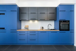 A contemporary kitchen with striking blue cabinets, a black backsplash, and built-in appliances.