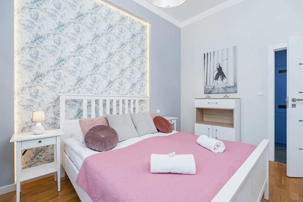 A cozy bedroom featuring a bed with pink bedding, decorative cushions, and a clean, light wall design.