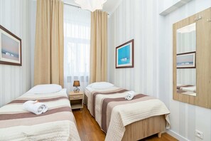 A bright room with two single beds, wooden furniture, and large windows allowing natural light to flow in.