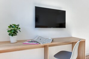 A small workstation with a wooden desk, a flat-screen TV mounted above, and a green plant for decoration. The area is simple yet practical.