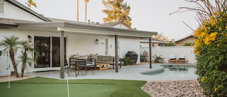 beautiful backyard w/ putting green, covered patio with comfortable seating & sparkling pool