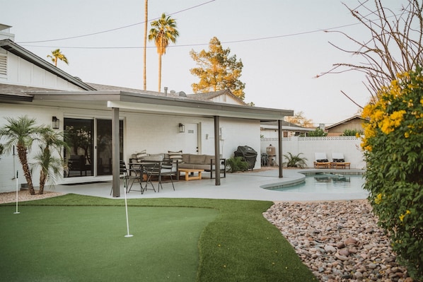 beautiful backyard w/ putting green, covered patio with comfortable seating & sparkling pool