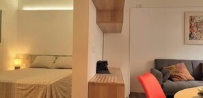 The apartment features a spacious bedroom with a comfortable queen-size bed, a stylish headboard, and soft linens. The bedroom is separated from the living area by a partial wall.