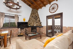 Open-plan living room with sofa, dining area, kitchen, ornamental fireplace, A/C, WiFi internet, and satellite TV