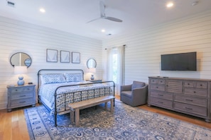The master suite features shiplap walls, a ceiling fan and night stands with reading lamps.