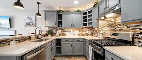 The open-concept kitchen has a gas stove, microwave, dishwasher, and fridge. It is fully stocked with all basic utensils. The  breakfast bar has three seats looking in to the kitchen.