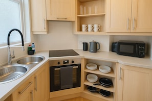 Bright, functional kitchen with a sleek, minimalist design. Light wood cabinetry, a built-in oven, electric cooktop, fridge with freezer compartment, washing machine and organized open shelving create a warm, practical space for cooking and dining.