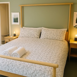 A cozy, peaceful bedroom with a large wooden bed, soft bedding, and natural light flooding in. Minimalist decor and warm bedside lamps create a calming retreat for your stay. Perfect for relaxing after a busy day.