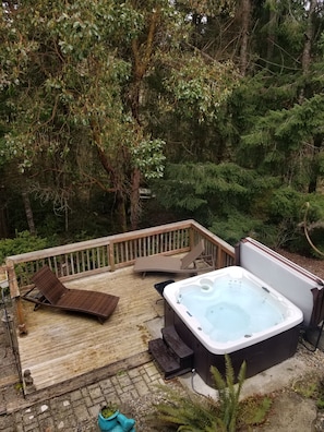 Hot tub and deck with lounge chairs under the branches and sky