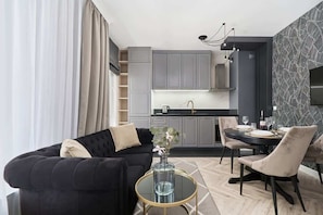 A spacious living room with black sofas, a glass coffee table, and stylish decor. Neutral tones on walls and floors contribute to a chic atmosphere.