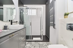 A modern bathroom featuring glass shower enclosures, patterned floor tiles, and a bright, clean aesthetic.