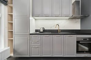 A contemporary kitchen with gray cabinetry, white countertops, and gold accents, including a sleek faucet. It includes modern appliances.