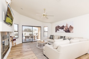 Bright open floor living space featuring a smart flat-screen TV, designer furnishings, and access to the outdoor patio with sparkling heated pool.