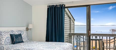 A queen-size bed adorned with a wall lamp, accompanied by a balcony offering a picturesque view of the beach.