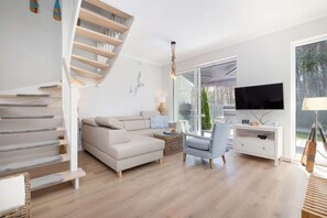 A spacious living room with a modern interior, including a sofa, armchair, and stairs leading to another level.