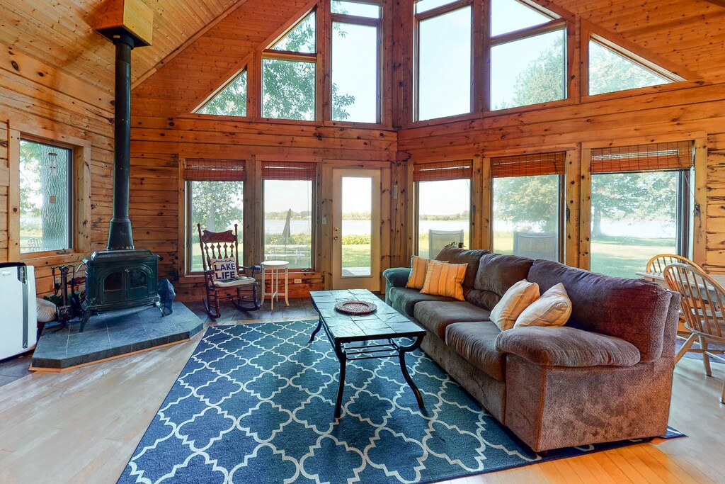 A lakefront Vermont cabin with floor to ceiling windows has a woodstove in the living room near a couch