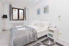 A bright bedroom with white walls and a double bed with white headboard and bedside tables.