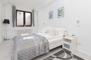A bright bedroom with white walls and a double bed with white headboard and bedside tables.