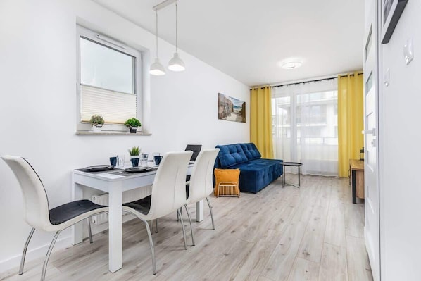 A bright living room featuring a dining table, chairs, and modern decor with large windows.