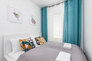A cozy bedroom with a soft bed, colorful cushions, and curtains in shades of white and teal.