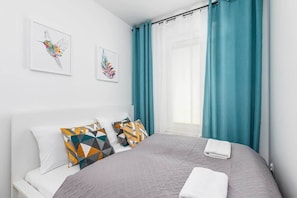 A cozy bedroom with a soft bed, colorful cushions, and curtains in shades of white and teal.