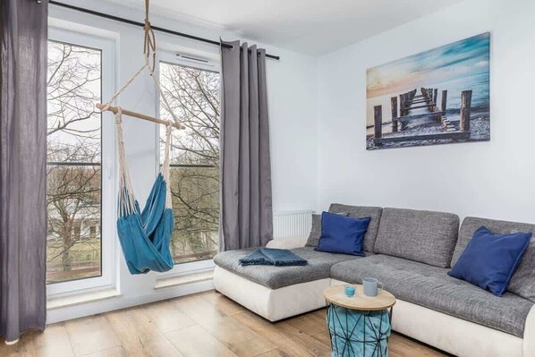 A modern living room in "Apartment Szpitalna 9," featuring a comfortable sofa, a coffee table, and large windows with blue accents.
