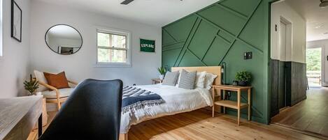 Green guest room with queen bed, sitting area, and work area