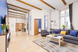 A spacious living room with a wooden floor, modern furniture, and large windows that let in natural light.