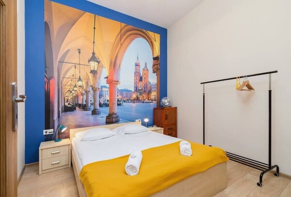 A cozy bedroom featuring a bed with a yellow blanket, a large poster on the wall, and a lamp.