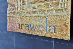 A close-up of a decorative wall sign with the word "Karawela" etched on it, likely referencing the apartment complex.
