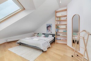 A cozy bedroom with slanted walls, a bed with light gray bedding, and a minimalist interior design.