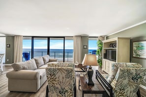The living room offers ample, comfortable seating with brand new sofa & recliners (Fall 2024), television, and expansive views of the Gulf of Mexico.