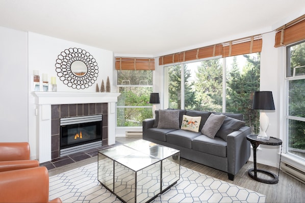 Open concept living area with gas fireplace and large bay windows overlooking the gardens