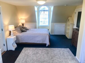 Primary Bedroom with queen bed, bureau, desk, tv, roku, and window AC unit.